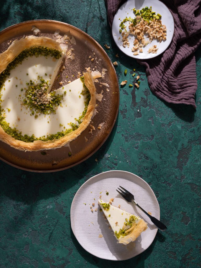 Baklava cheesecake sliced on a plate. Next to it, a piece of cake on a small plate. 