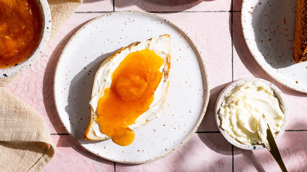 Brötchen mit Frischkäse und Aprikosenmarmelade, serviert auf einem Frühstückstisch.