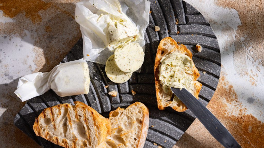 Za'atar-Butter liegt aufgeschnitten auf einem Brett mit geröstetem Brot.