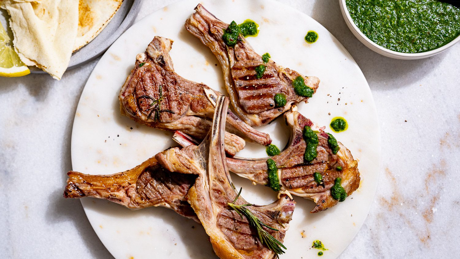 Grilled lamb chops on a plate. Next to it is green sauce and flatbread.