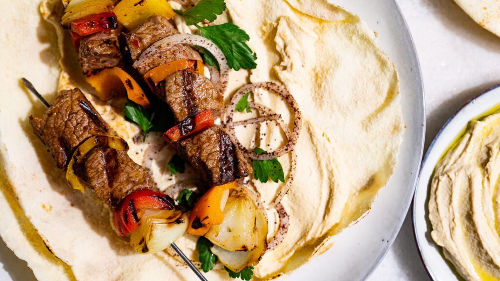 Shish kebab servido en un pan plano untado con hummus.