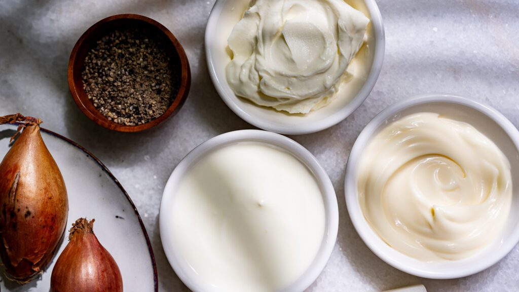 Cream cheese, sour cream and mayo in small bowls as ingredients for spinach and artichoke dip.