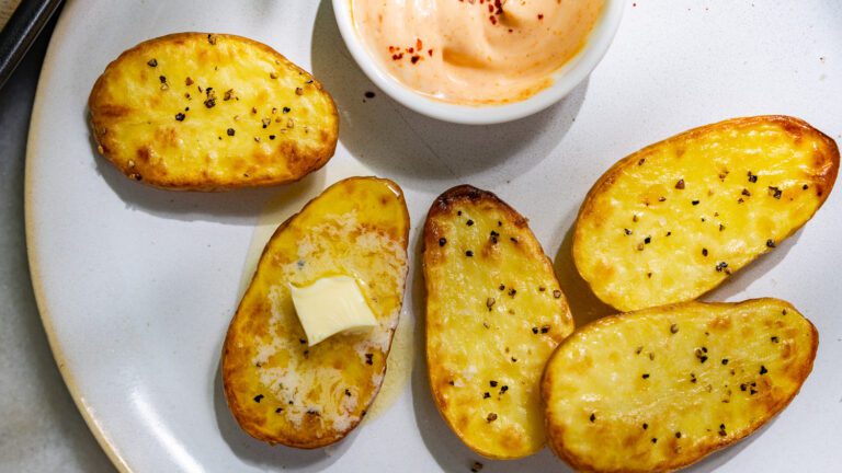 Golden baked potatoes with spicy mayo served on a plate.