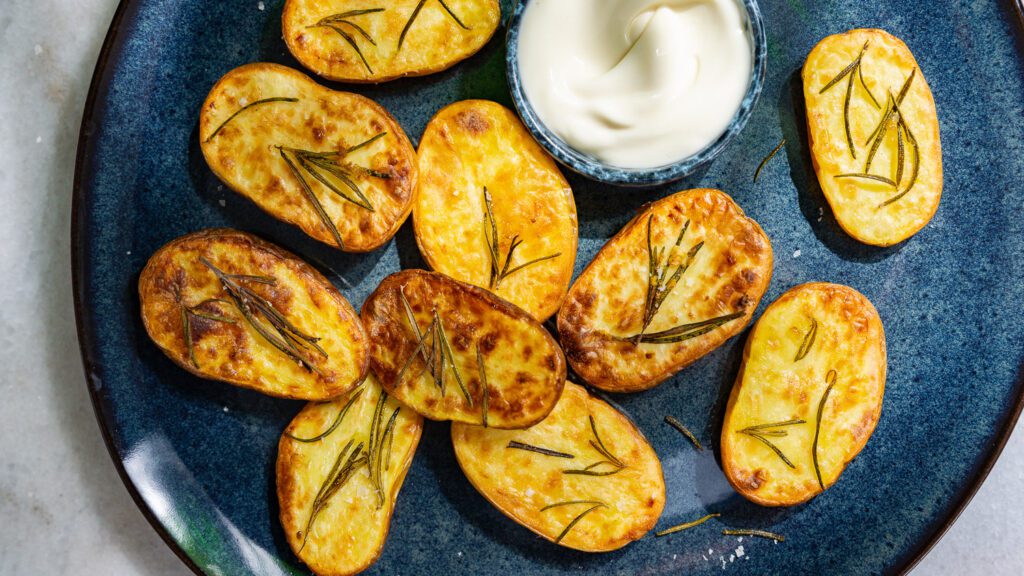 Patatas al romero de la freidora de aire caliente servidas en un plato con mayonesa.