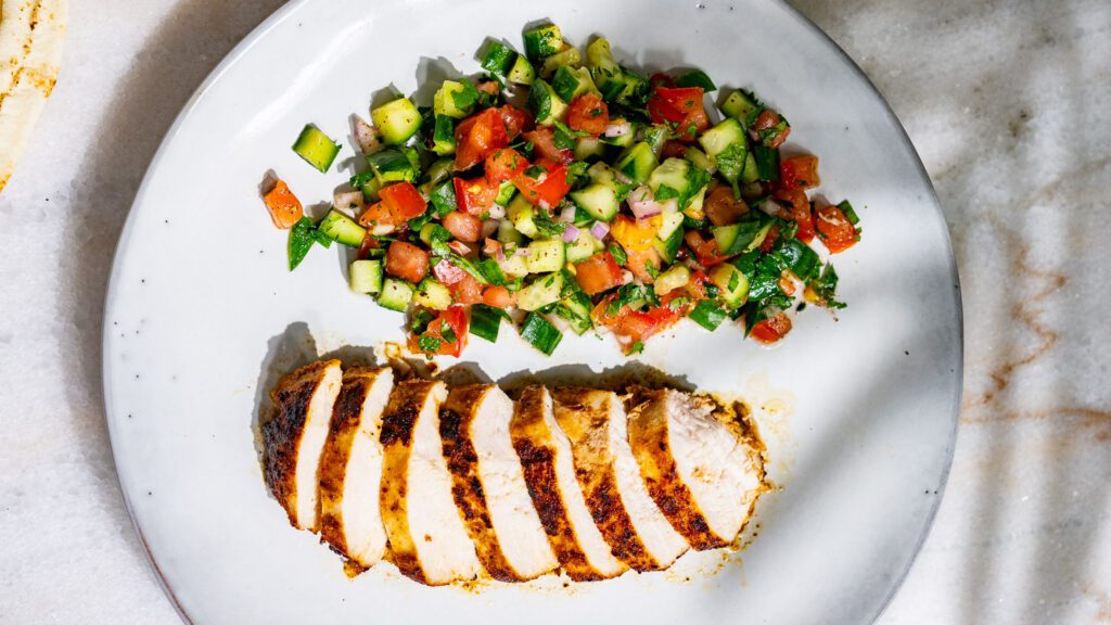 Tomato and cucumber salad with grilled chicken breast served on a plate.