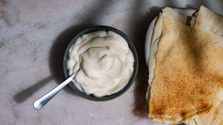 Toum servido com uma colher numa tigela. Ao lado, o pão achatado libanês.