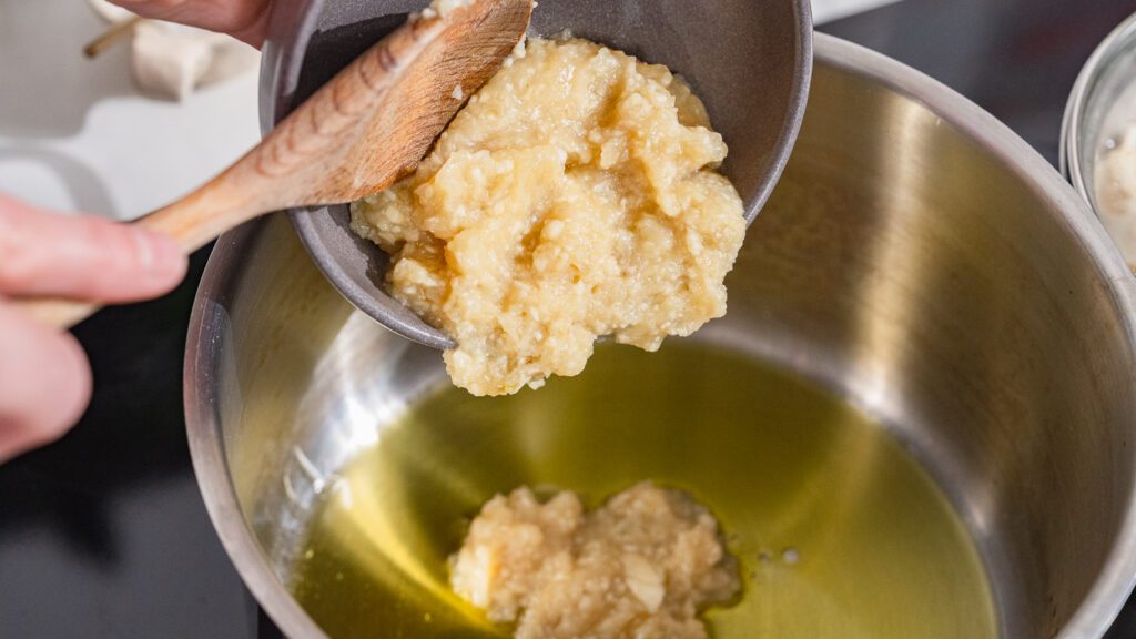 Knoblauch-Zwiebel-Paste wird zum Anbraten für Molokhia in einen Topf mit Öl gegeben.