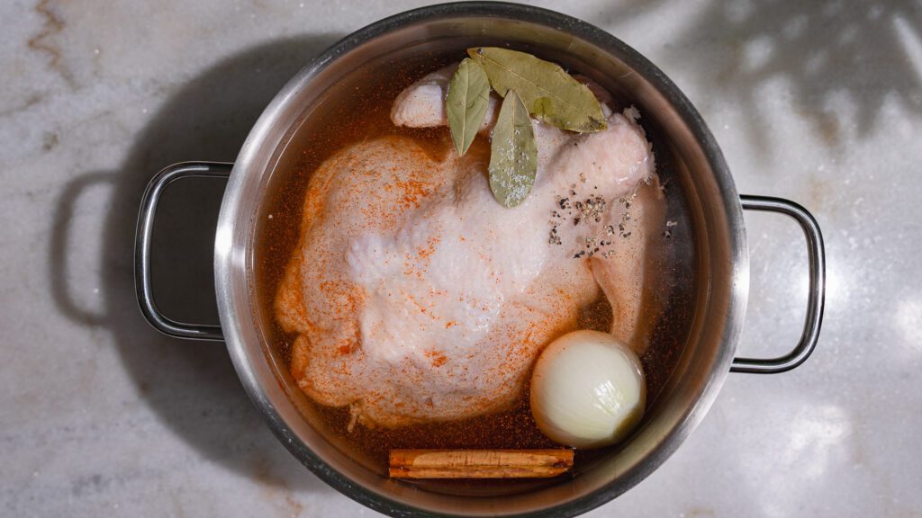 Suppenhuhn für Molokhia mit Zwiebel, Lorbeer, Zimstange und Gewürzen in einem Topf.