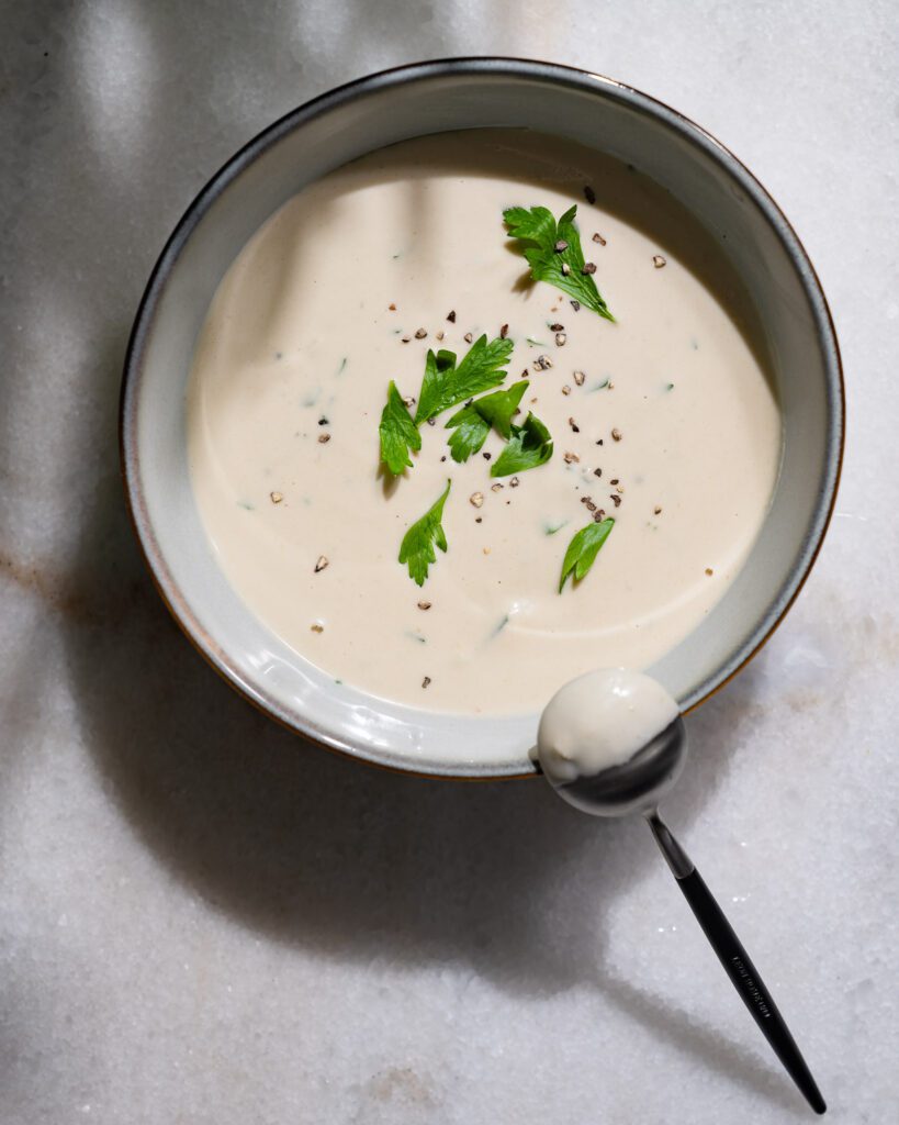 Tahini Sauce in einer Schüssel. Am Rand liegt ein kleiner Löffel.