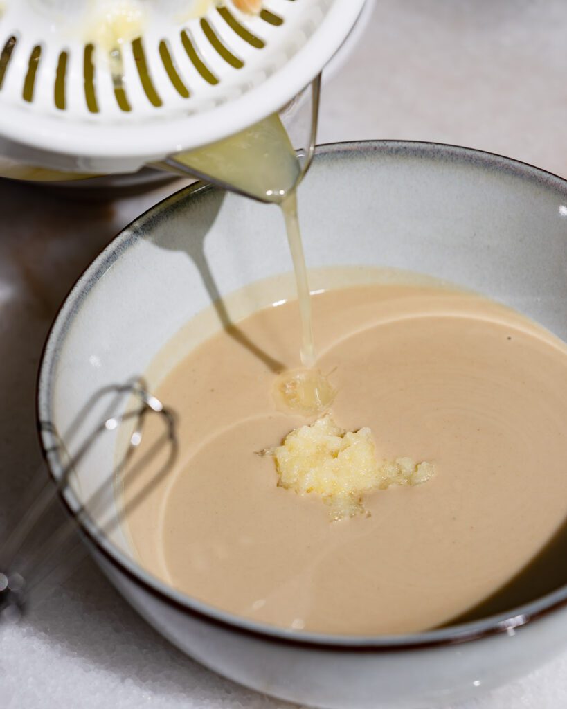 Für die Tahini Sauce wird Zitronensaft zum Knoblauch und Tahini gegossen.